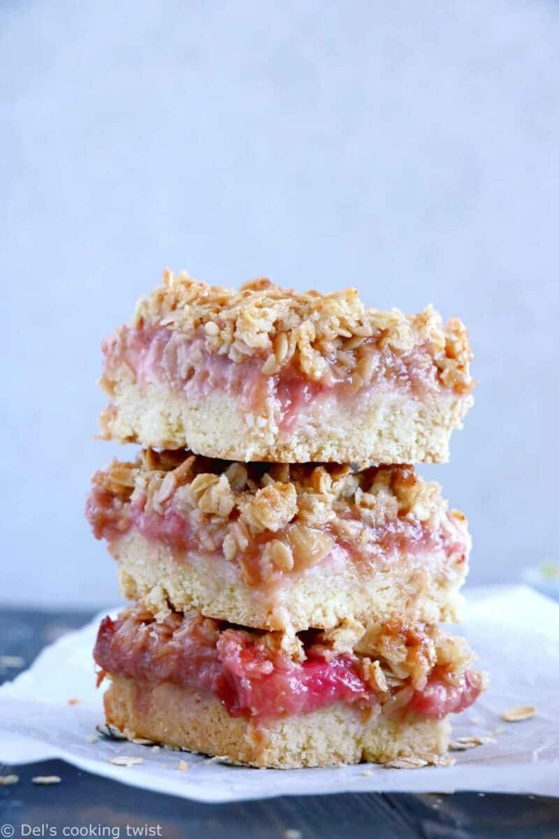 Golden-brown rhubarb crumble bars stacked on parchment paper, with a focus on the crumbly topping.