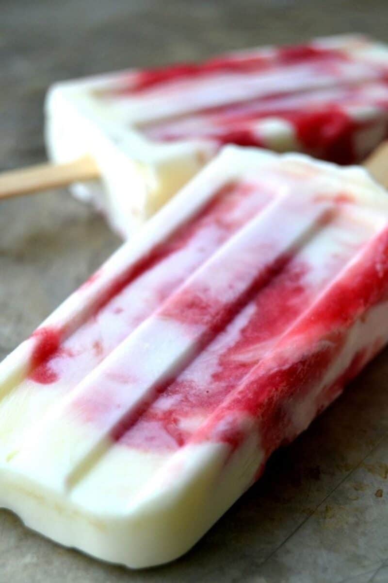 Icy rhubarb and Greek yogurt popsicles with visible rhubarb pieces, arranged on a rustic wooden surface.
