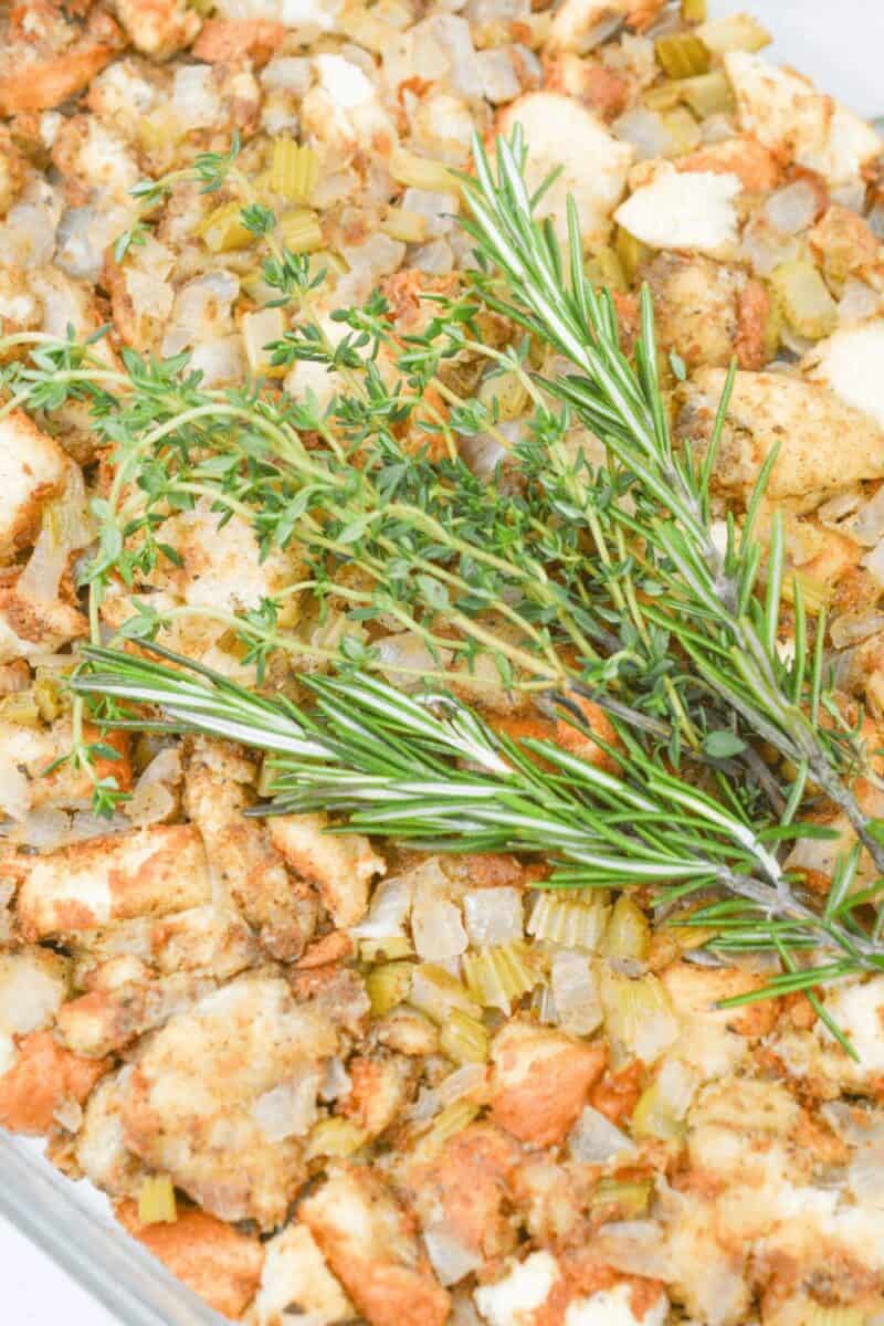 Close-up of traditional Thanksgiving stuffing in a glass dish, garnished with fresh rosemary and thyme sprigs on top.