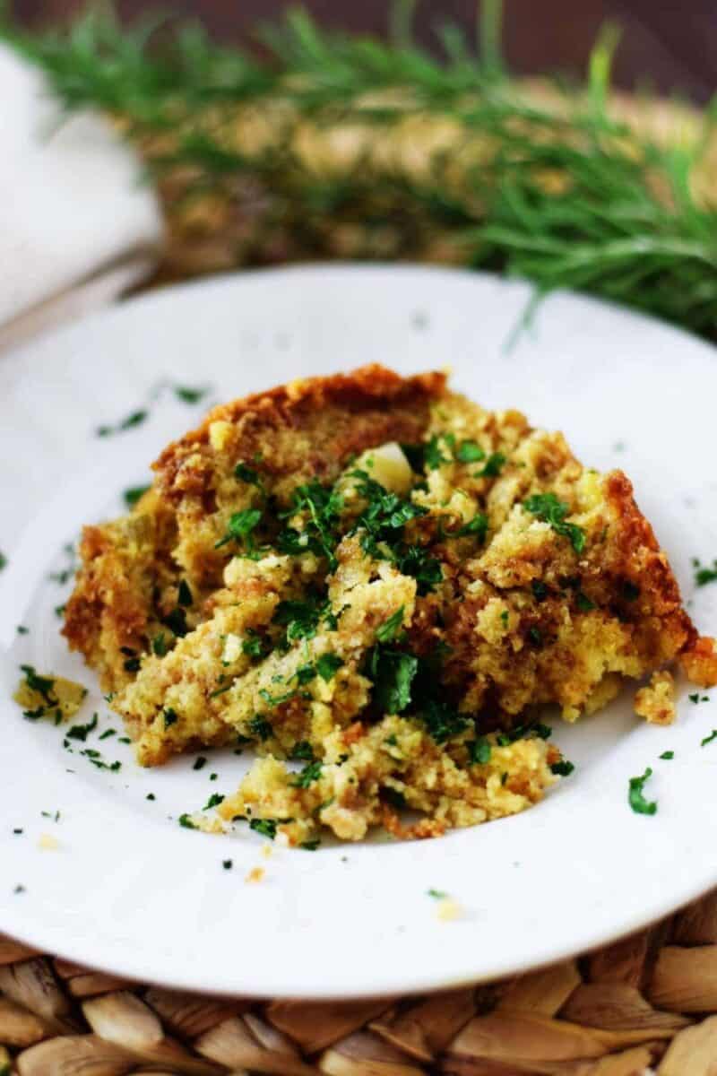 A plate of Thanksgiving stuffing is garnished with fresh, chopped parsley, showcasing a golden-brown crust and fluffy interior.