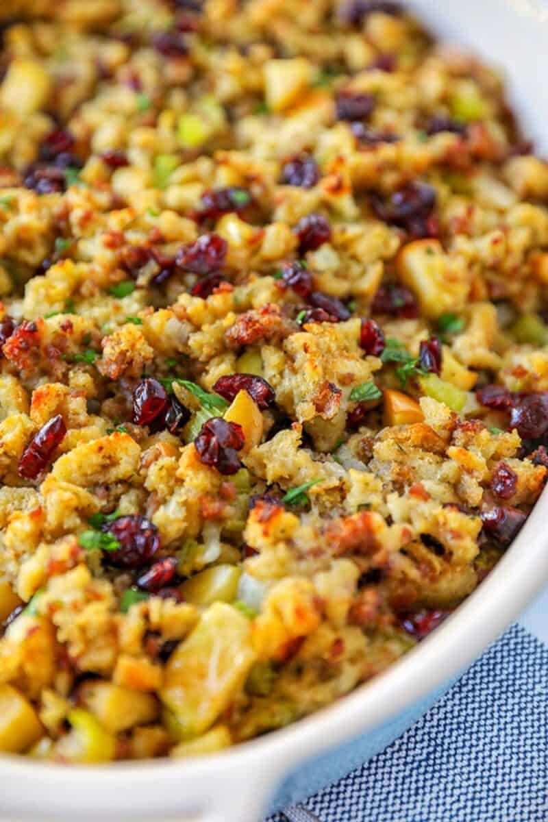 Close-up of a festive stuffing dish with cranberries and diced apples adding a pop of color among the seasoned bread cubes.