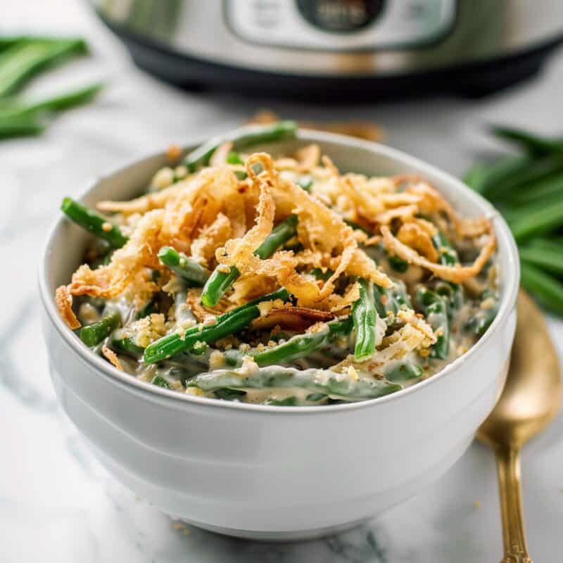 A bowl of Crockpot Green Bean Casserole with green beans and crispy fried onions, placed in front of a slow cooker.