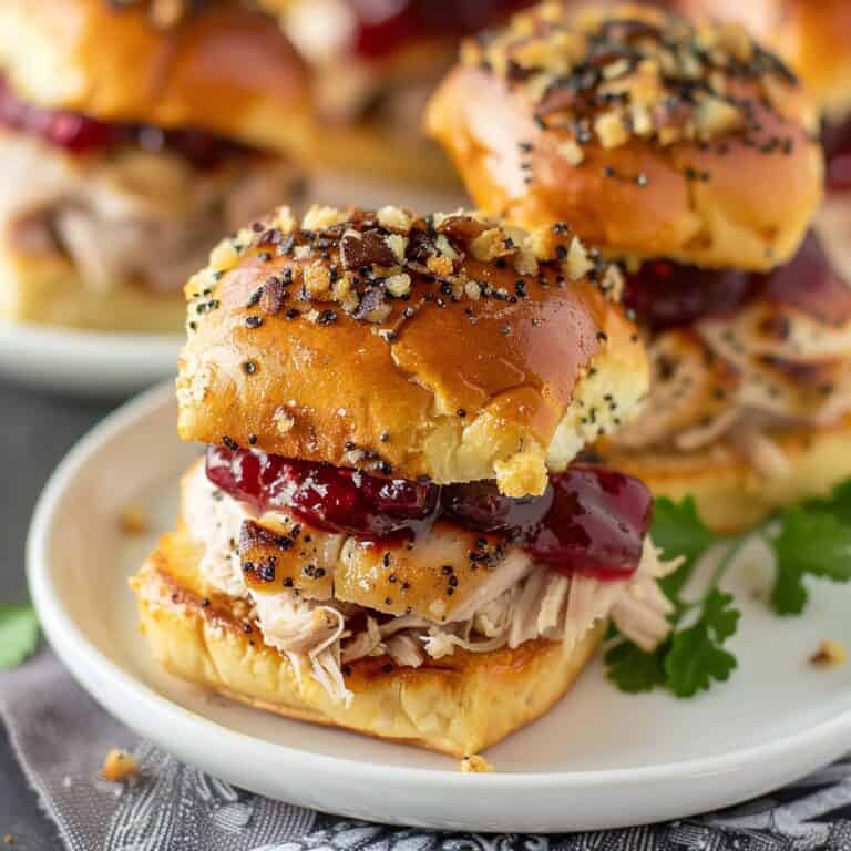 Delicious Leftover Turkey Sliders topped with cranberry sauce and Swiss cheese, served on sweet rolls, drizzled with a buttery mustard and garlic sauce, and garnished with poppy seeds and dehydrated onions.