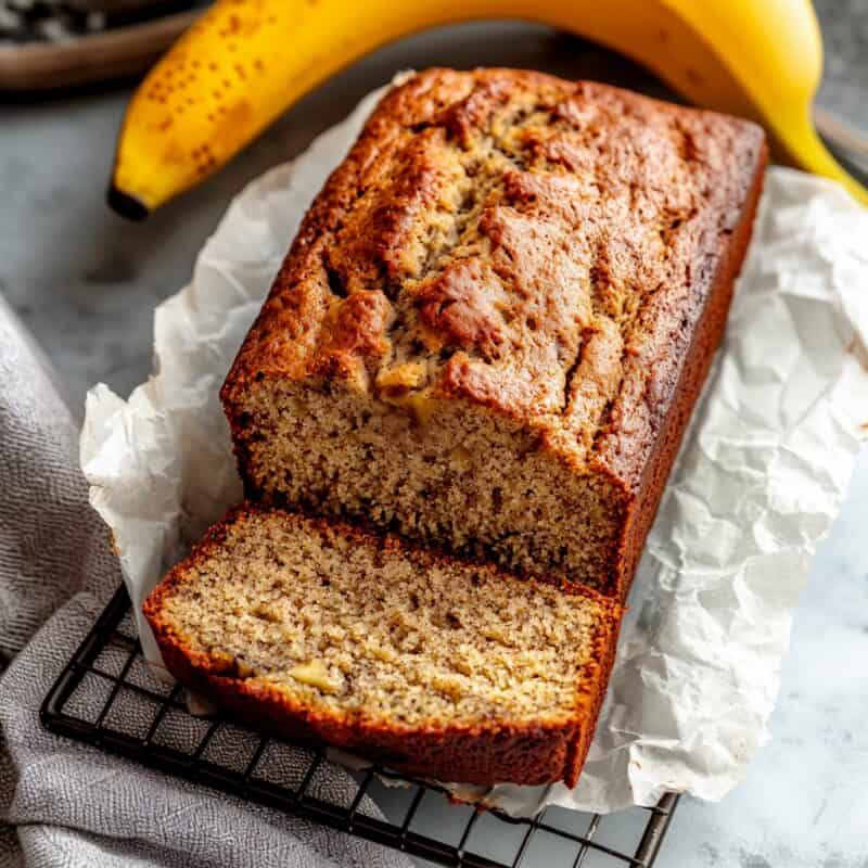 Freshly baked gluten-free banana bread loaf sliced, revealing the soft, moist texture of the bread, placed on a cooling rack with parchment paper.