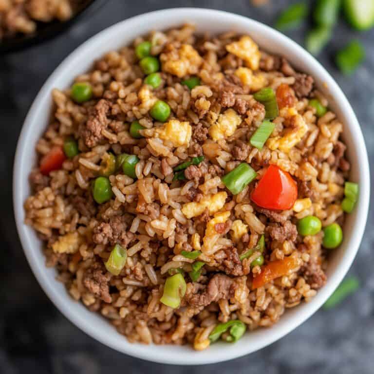 A bowl of ground beef fried rice with peas, diced red bell pepper, scrambled eggs, and green onions on top. The rice looks fluffy and well-seasoned, with vibrant colors from the vegetables.