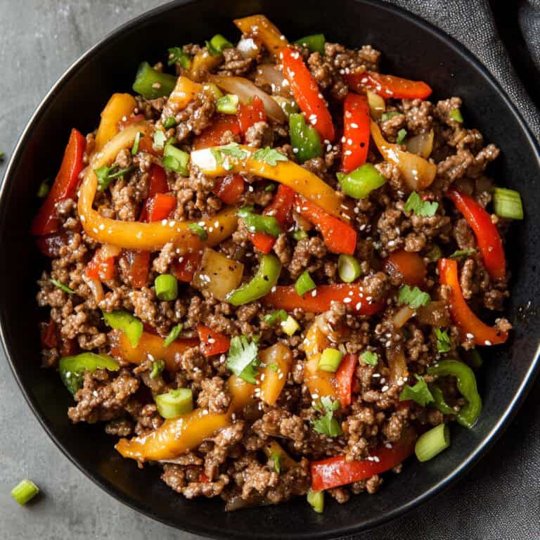 A colorful bowl of low-carb ground beef stir fry with red, yellow, and green bell peppers, topped with sesame seeds and chopped green onions. A delicious and flavorful keto-friendly stir fry perfect for a quick dinner.