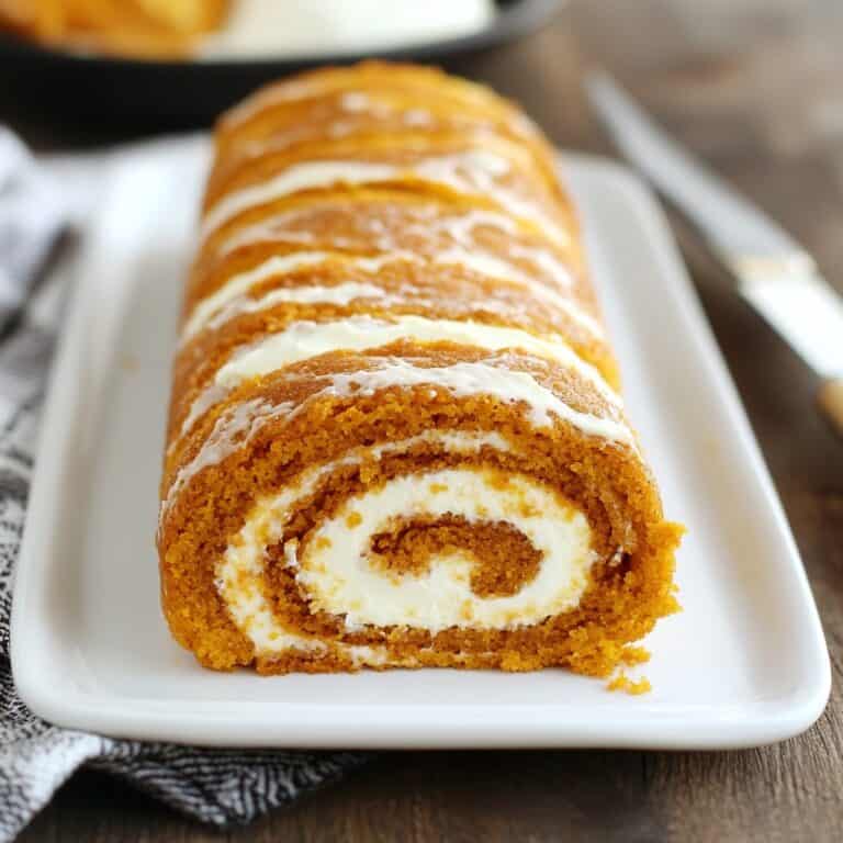 Pumpkin Roll: A rolled pumpkin cake with visible swirls of cream cheese filling, sliced on a platter. A festive pumpkin dessert ideal for holiday celebrations.