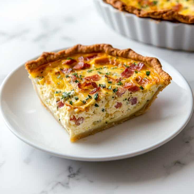 A slice of Mississippi Sin Quiche on a white plate, featuring a golden, flaky crust filled with a creamy mixture of ham, cheese, and green onions, topped with crispy bacon and parsley.