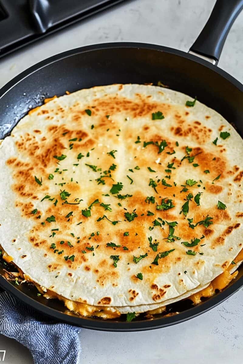 A full buffalo chicken quesadilla cooking in a nonstick skillet, garnished with chopped parsley