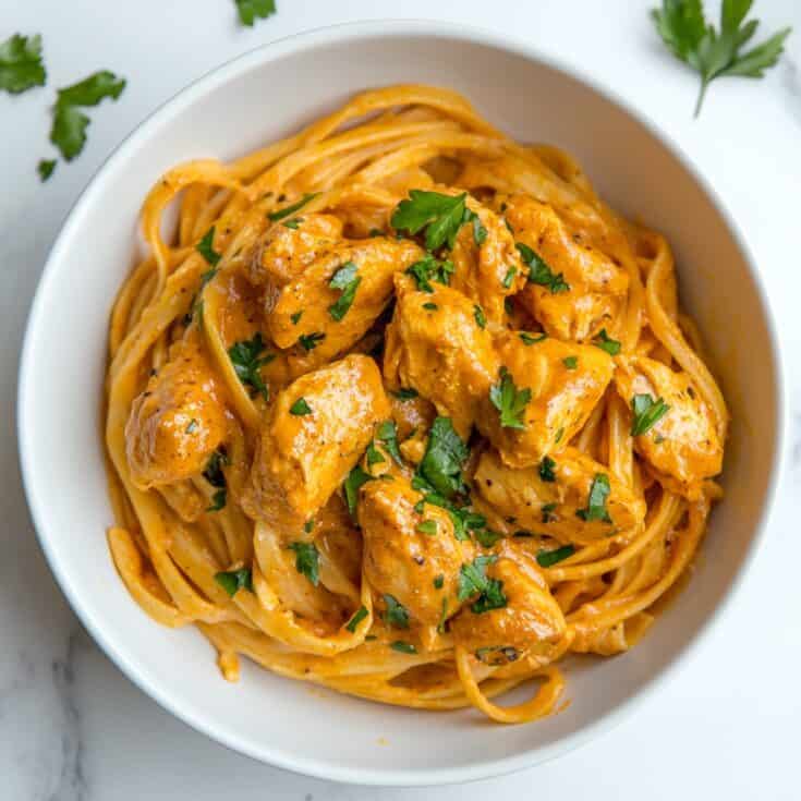 Close-up of creamy butter chicken linguini served in a white bowl and garnished with fresh parsley.