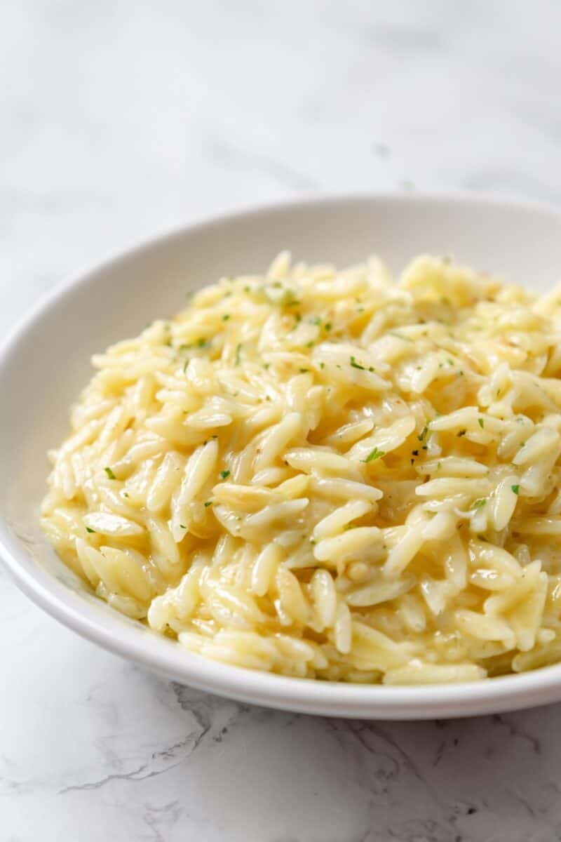 Close-up side view of creamy cottage cheese orzo served in a white bowl on a marble surface, garnished lightly with herbs.