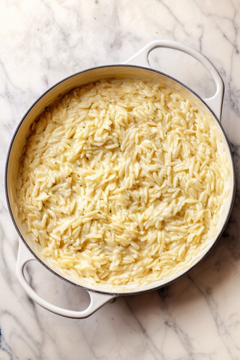 Overhead view of creamy cottage cheese orzo in a white Dutch oven on a marble surface, showing its rich and glossy texture.