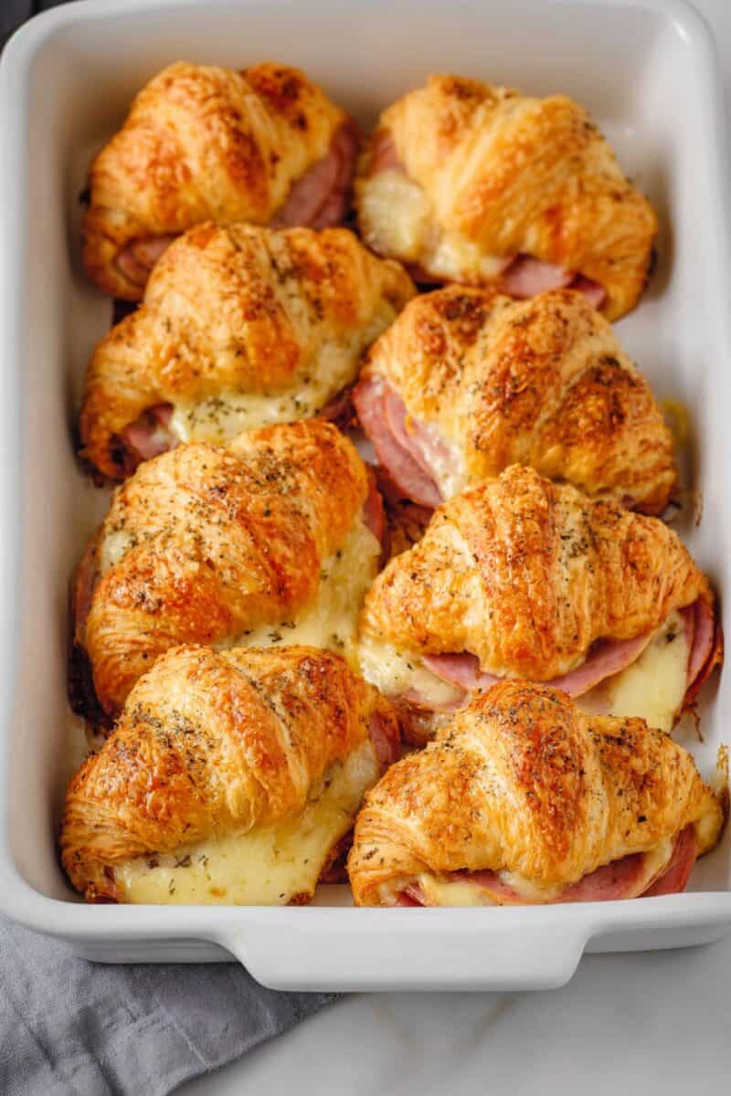 Overhead view of golden baked ham and cheese croissants in a white baking dish