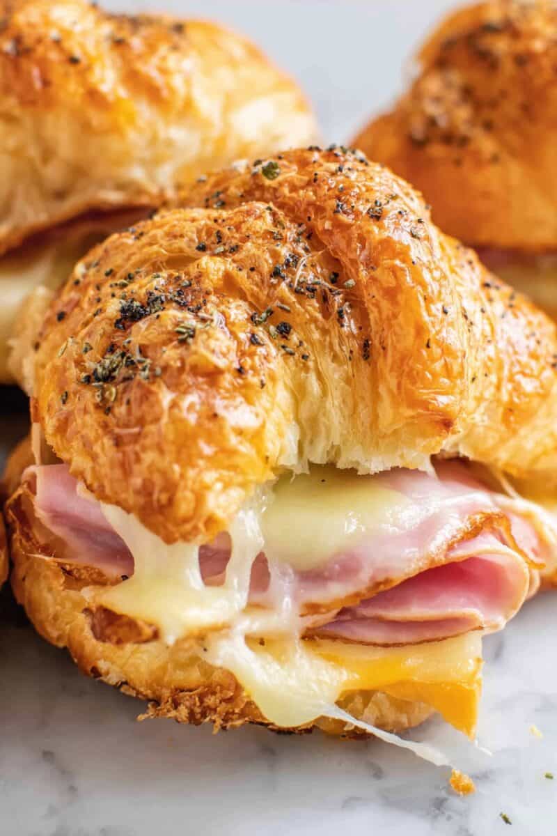 Close-up of a flaky ham and cheese croissant with gooey melted cheese and toasted herbs on top.