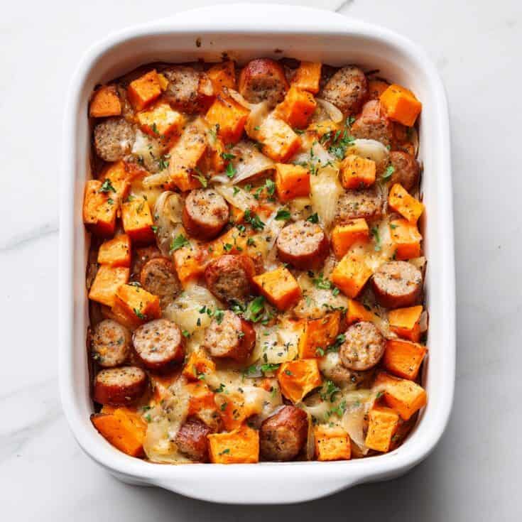 Overhead view of sweet potato apple chicken sausage bake in a white ceramic baking dish, showcasing golden sausage and caramelized sweet potatoes.
