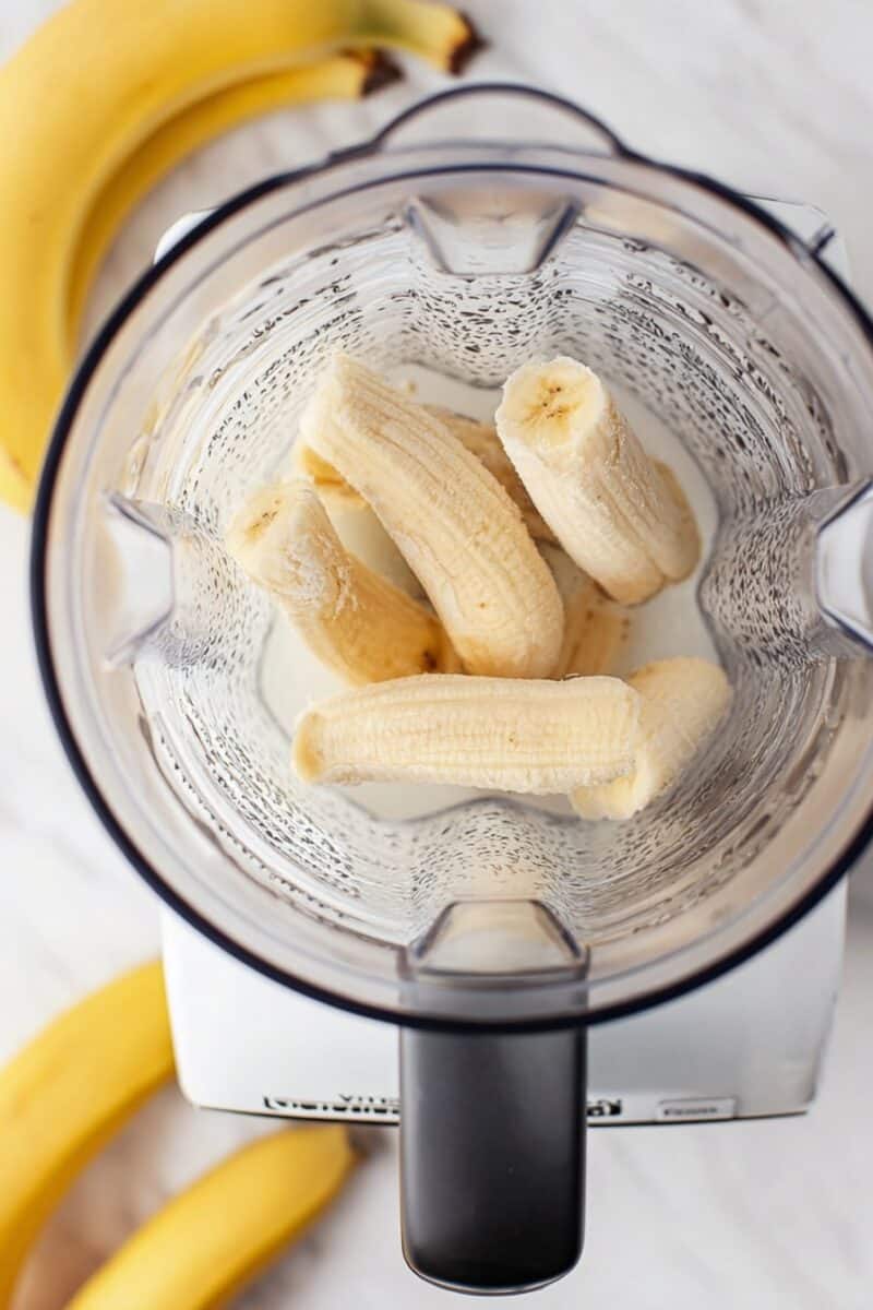 Overhead view of a blender with peeled bananas inside, showing the first step of making banana milk.