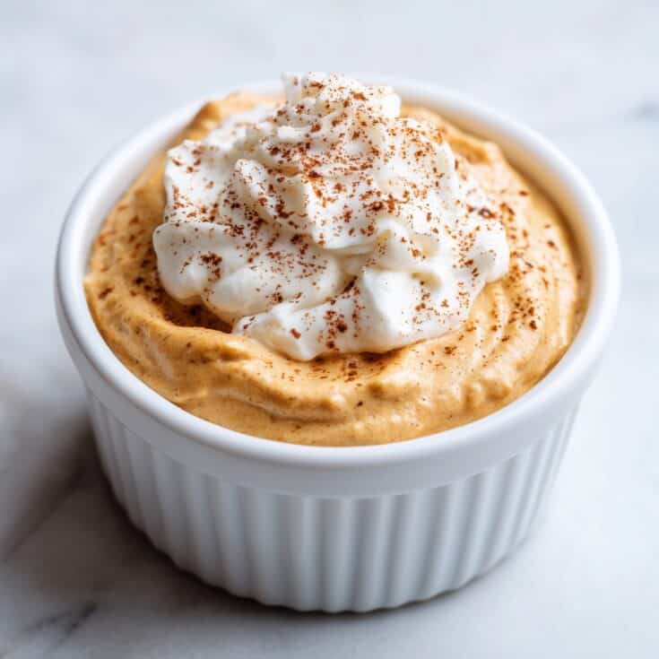 Pumpkin fluff pudding in a white ramekin topped with whipped cream and cinnamon