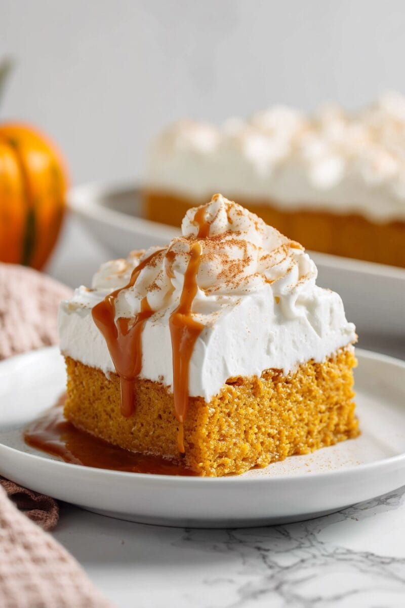 Pumpkin Tres Leches Cake topped with piped whipped cream and caramel, with the full cake in the background — perfect for Thanksgiving dessert tables.