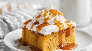 A moist slice of Pumpkin Tres Leches Cake served on a white plate, topped with whipped cream and caramel — a fall dessert favorite.