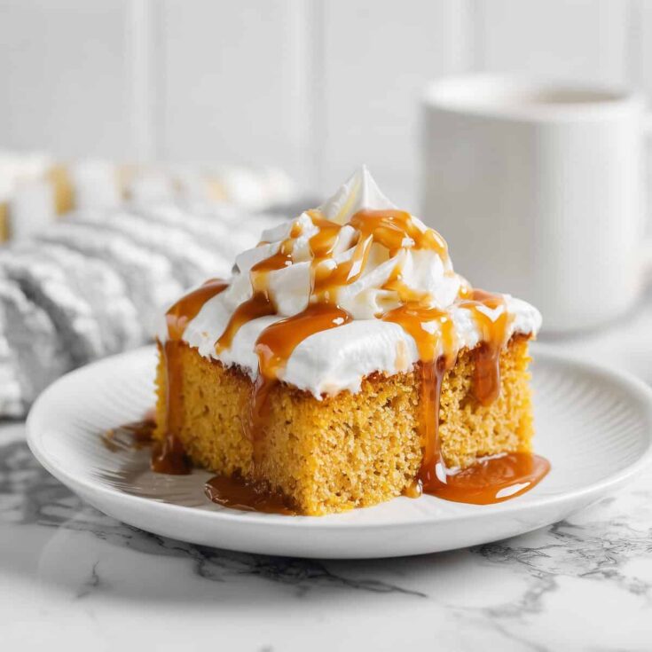 A moist slice of Pumpkin Tres Leches Cake served on a white plate, topped with whipped cream and caramel — a fall dessert favorite.