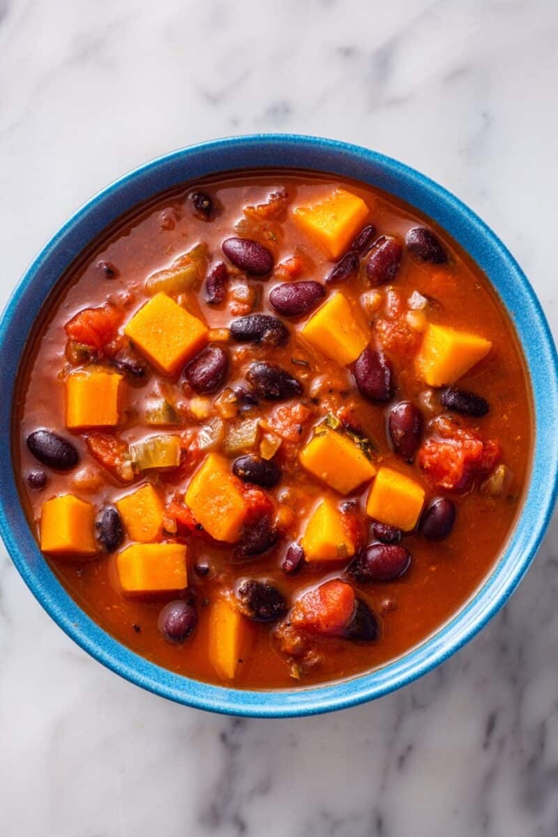 Top-down view of vegetarian butternut squash and sweet potato chili with beans in a tomato broth.