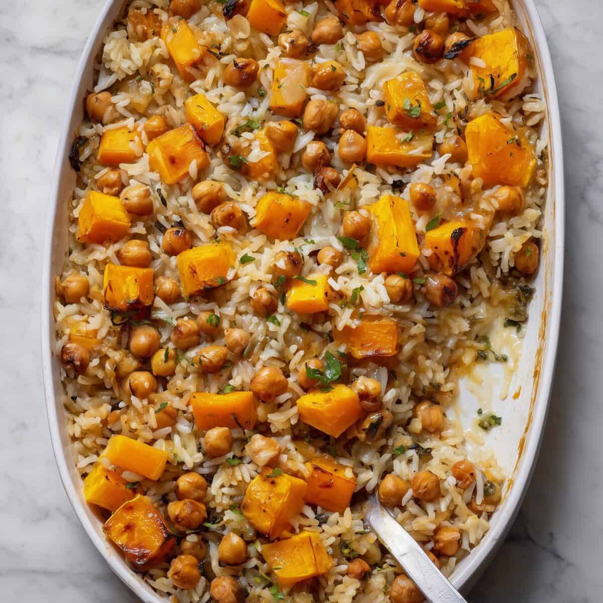 Overhead view of a vegan roasted butternut squash and chickpea rice bake in a white casserole dish, showing golden squash cubes, crispy chickpeas, and fluffy rice.