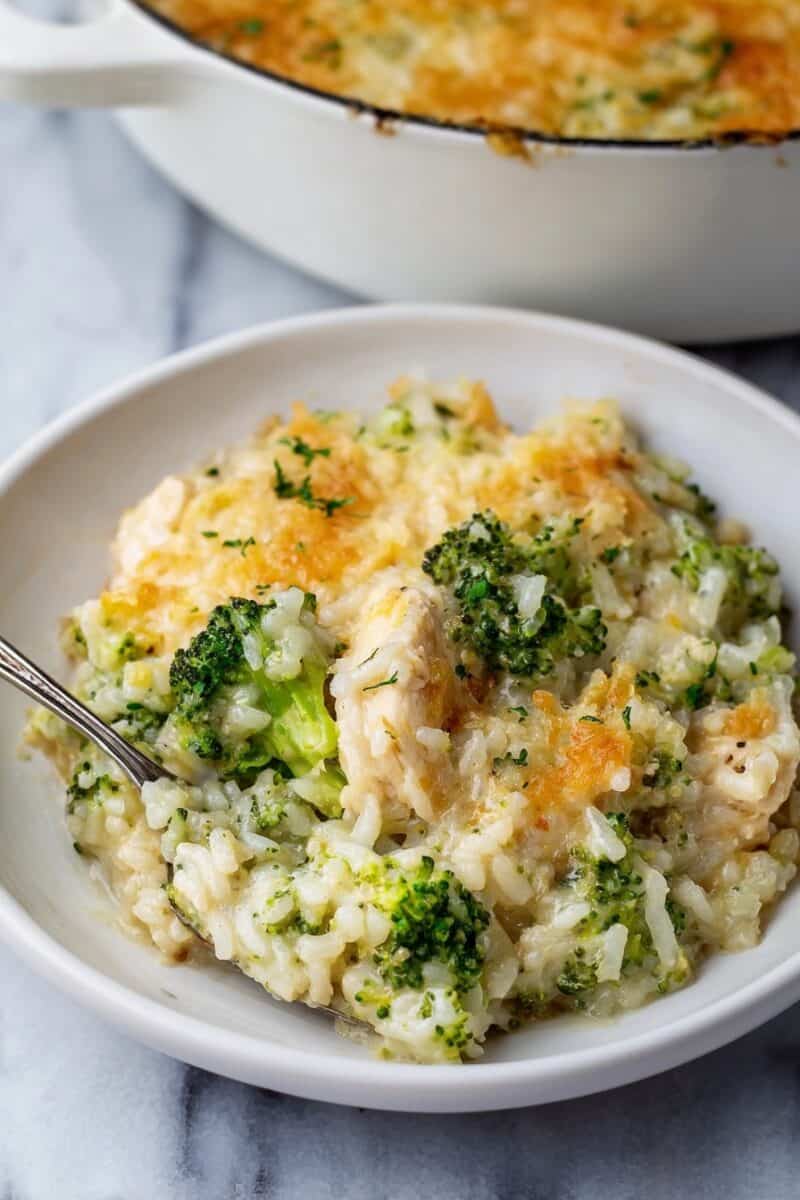 Creamy chicken broccoli rice casserole served in a white bowl, topped with melted cheddar and parsley, with the baking pan in the background.