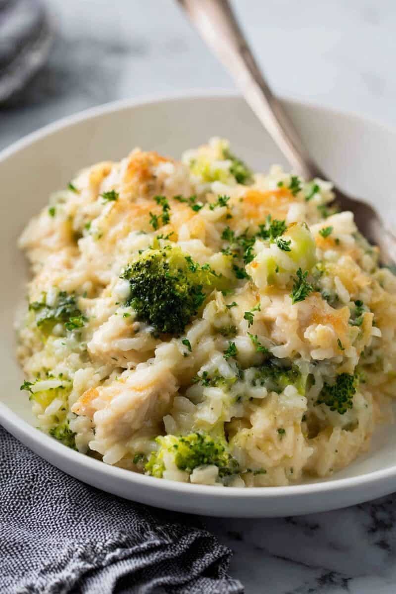 Warm chicken broccoli rice casserole with gooey cheese and tender rice, served in a white bowl with a fork ready to dig in.