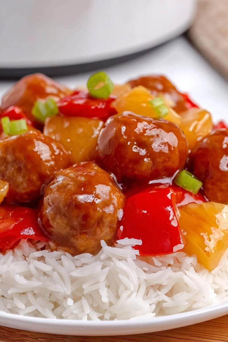 Sweet and sour chicken meatballs with pineapple chunks and red bell peppers in thick sauce served over white rice.