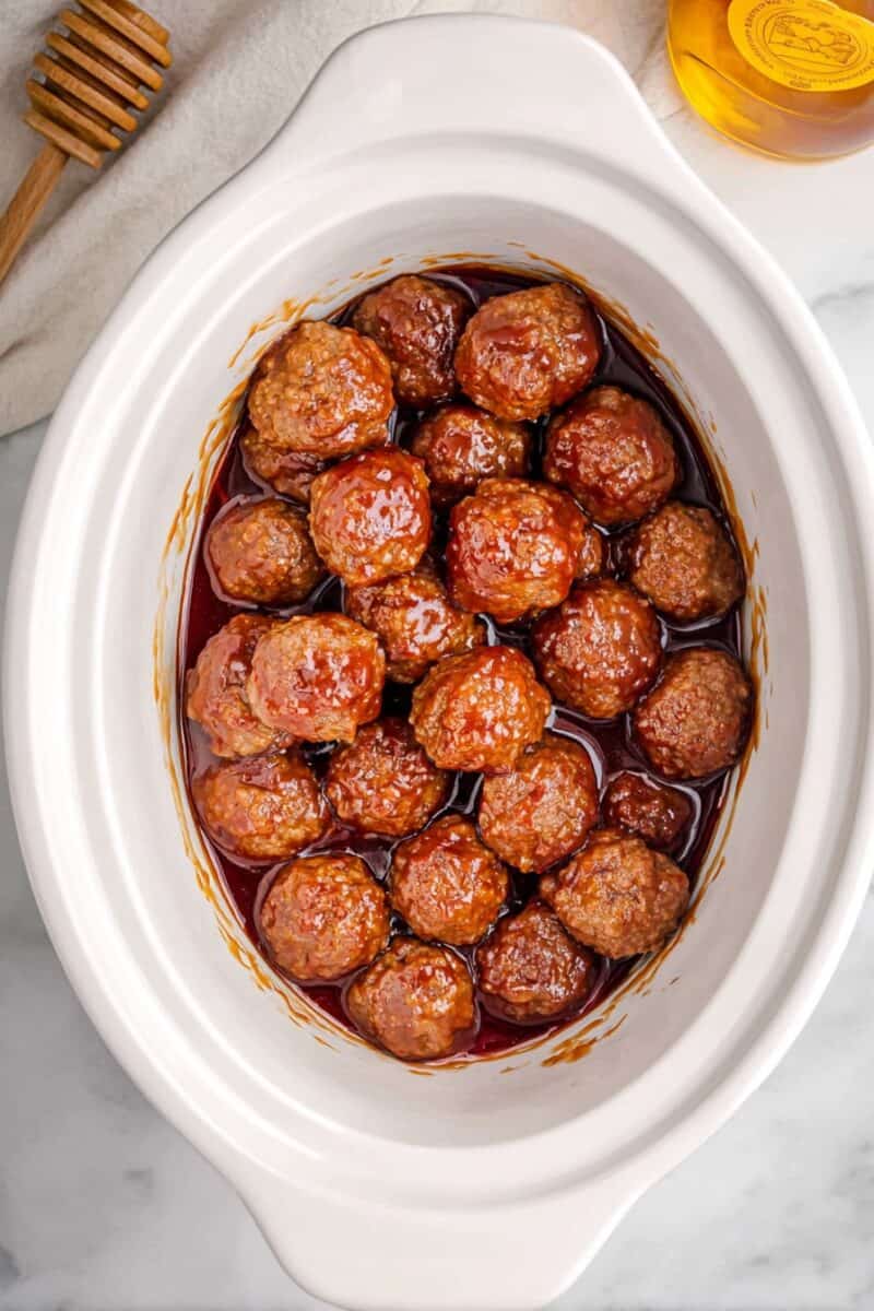 Overhead view of Crockpot Honey BBQ Meatballs coated in a thick, glossy sweet barbecue sauce inside a white slow cooker, with meatballs fully covered and evenly glazed.