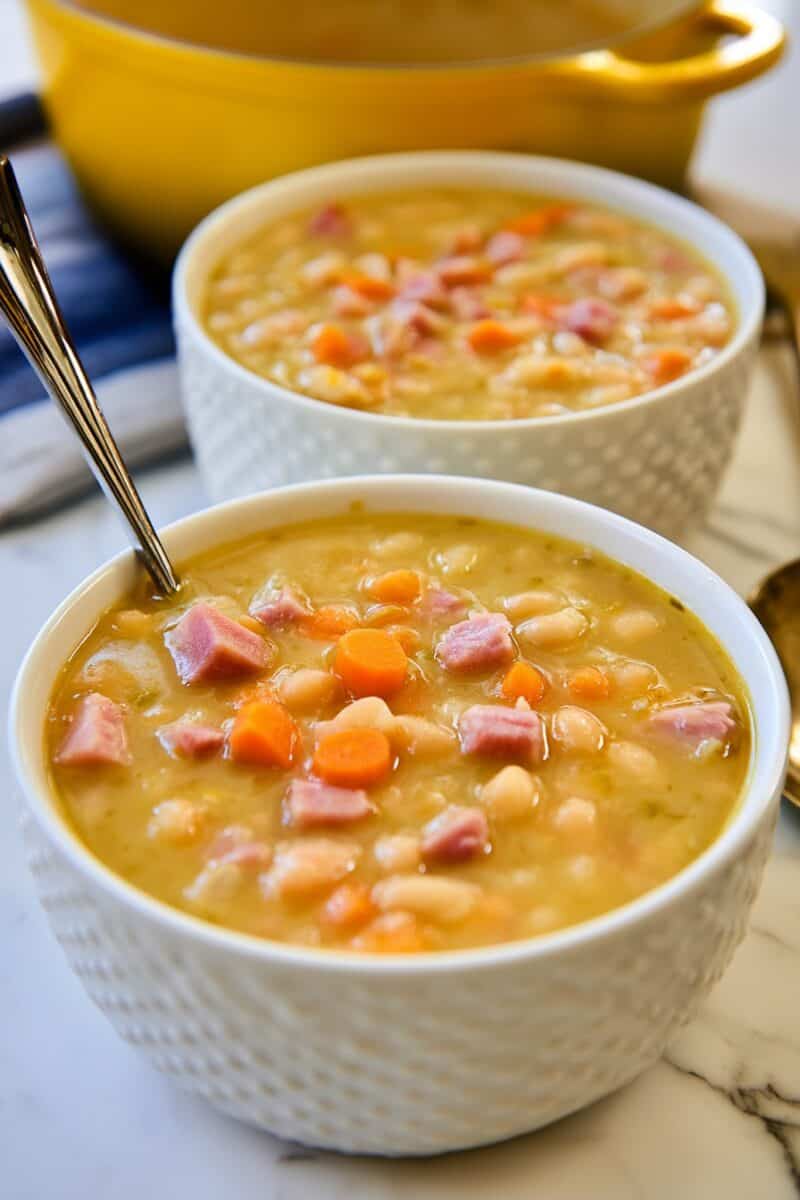 Two white bowls filled with ham and bean soup made with diced ham, white beans, carrots, and a savory broth.